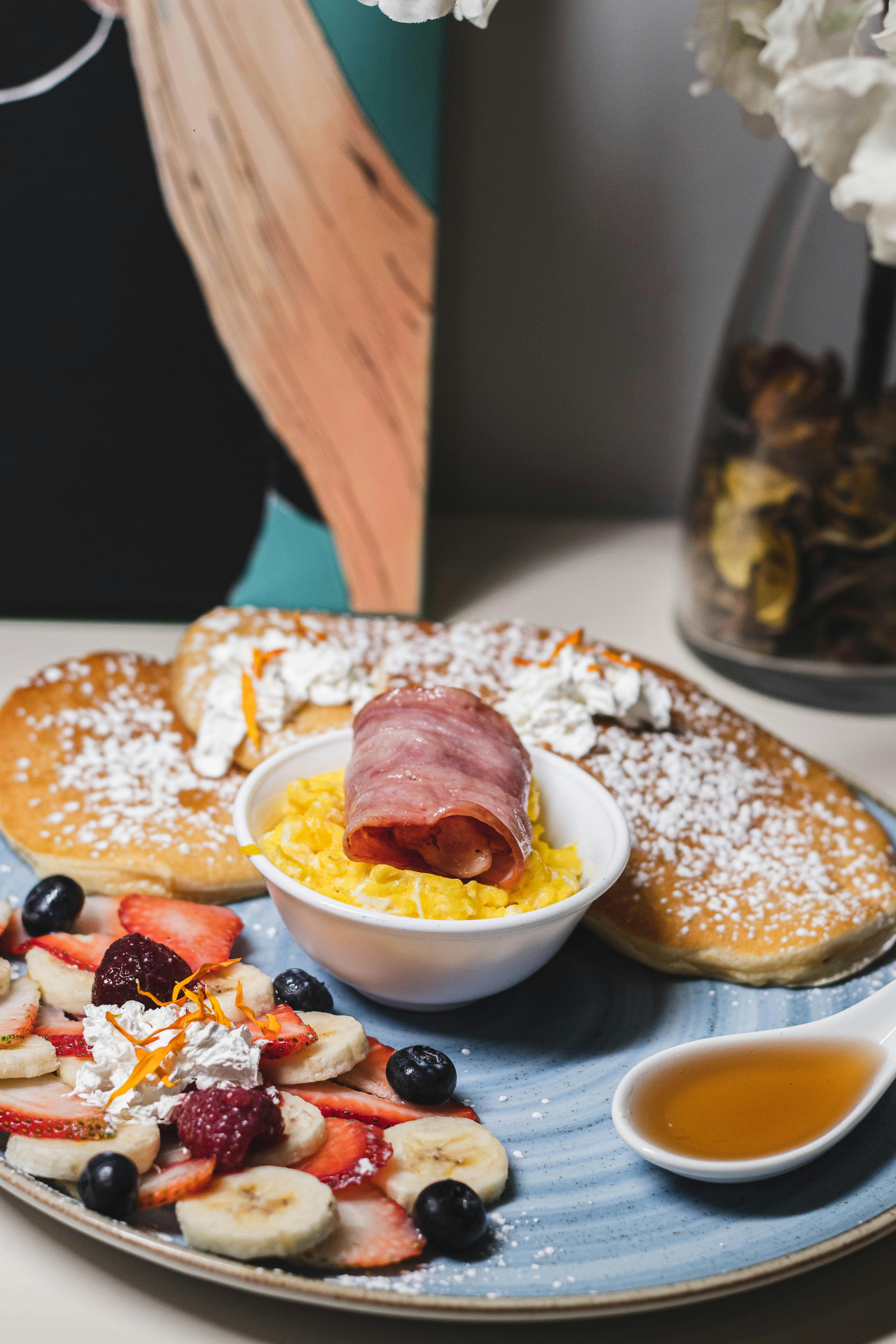 A delightful breakfast setup featuring pancakes, fruit slices, scrambled eggs, and syrup.