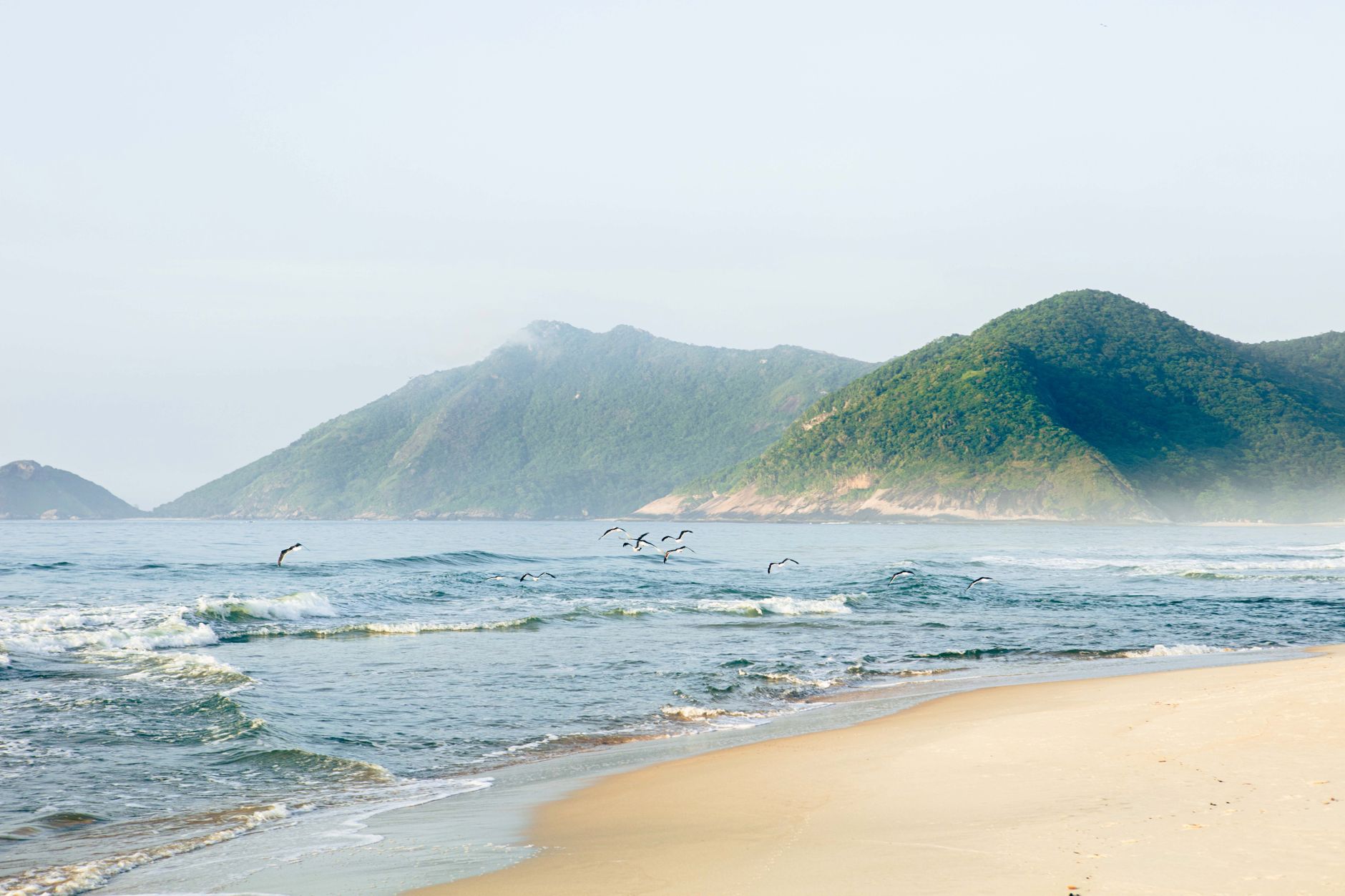 Peaceful beach scene with waves and distant mountains under a clear sky.