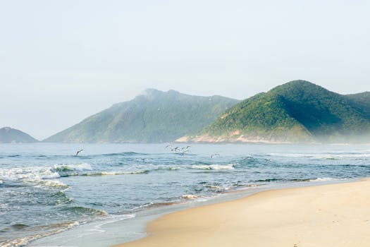 Peaceful beach scene with waves and distant mountains under a clear sky.