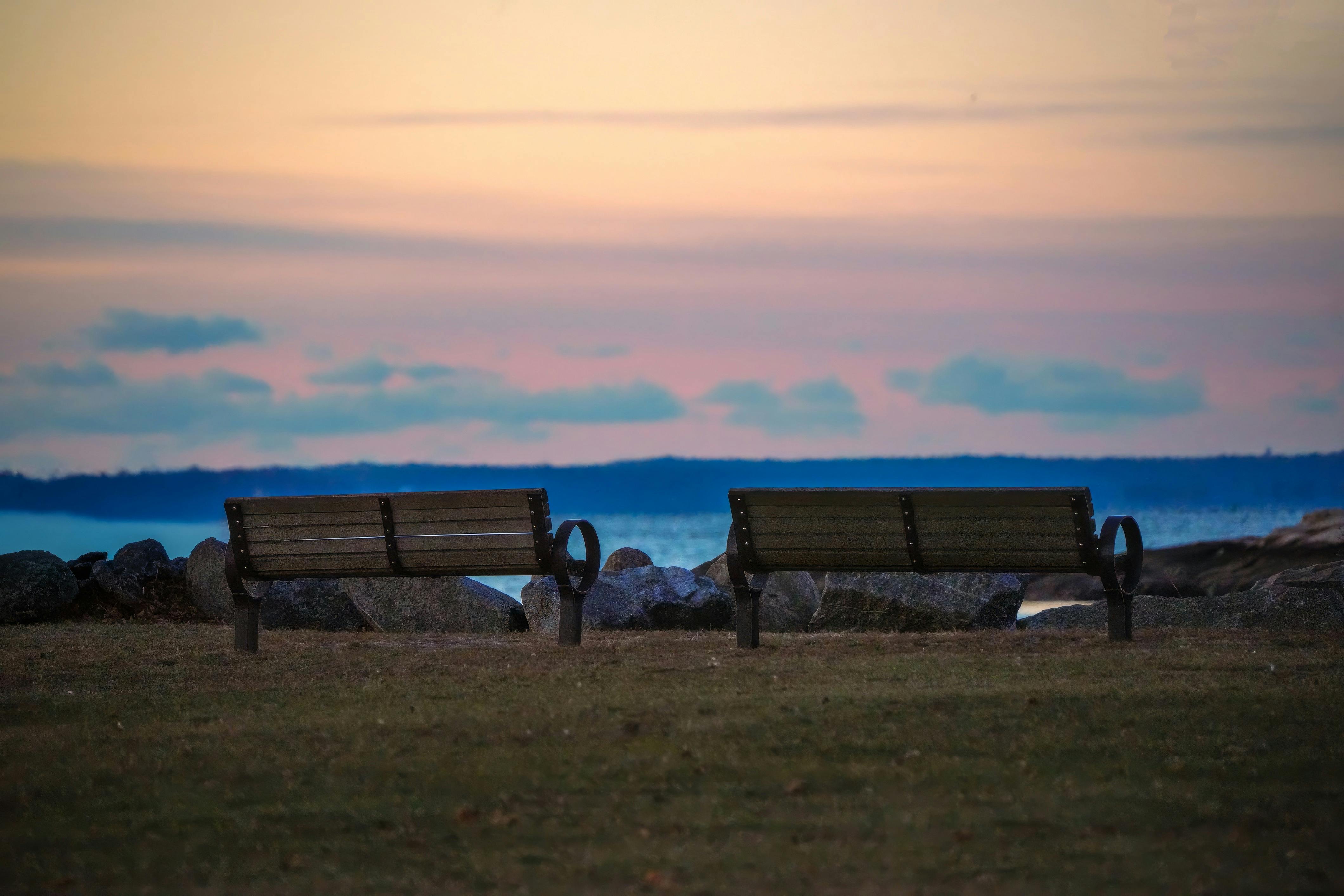 日落时分，两张空荡荡的长椅面向大海，营造出一种宁静祥和的氛围。