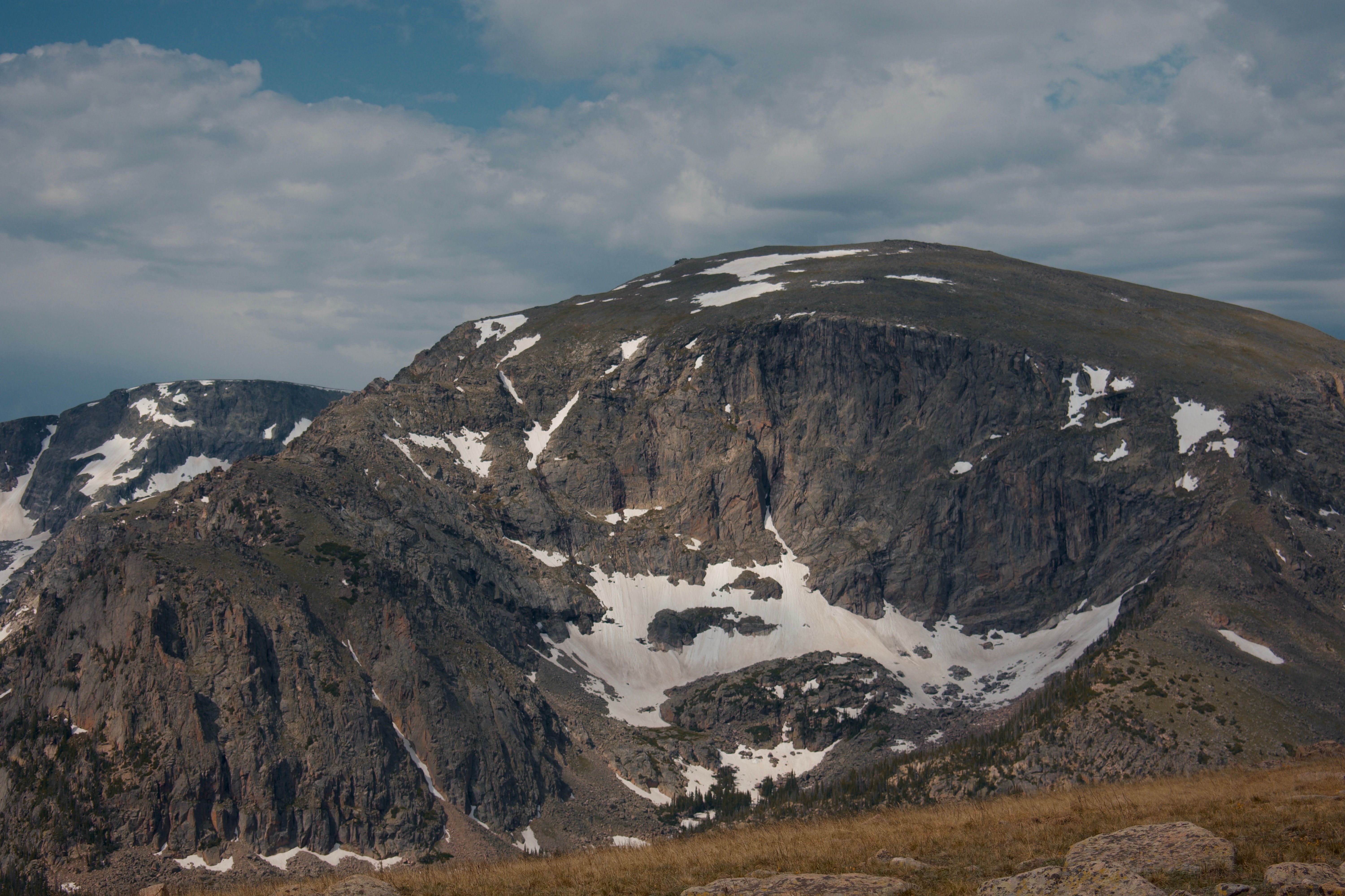 Scenic view of a rocky mountain with snow patches and a cloudy sky in a natural landscape.