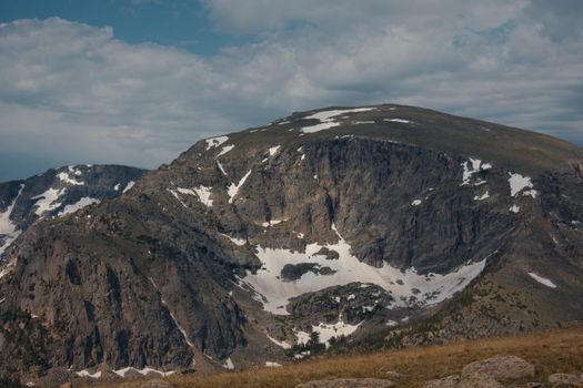 Scenic view of a rocky mountain with snow patches and a cloudy sky in a natural landscape.