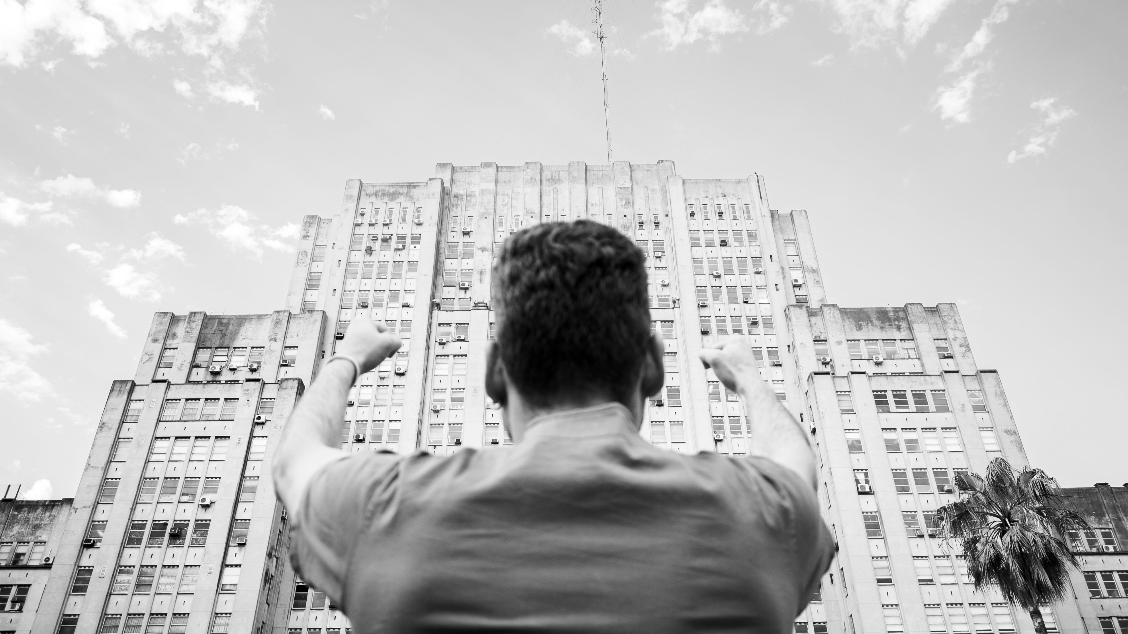 Black and white image of a person raising fists in celebration against a grand building backdrop in Buenos Aires.