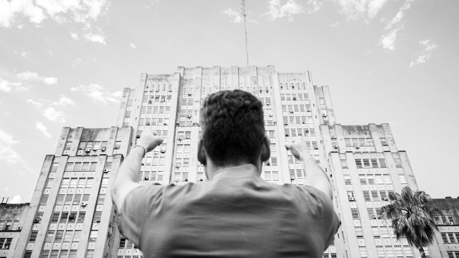 Black and white image of a person raising fists in celebration against a grand building backdrop in Buenos Aires.