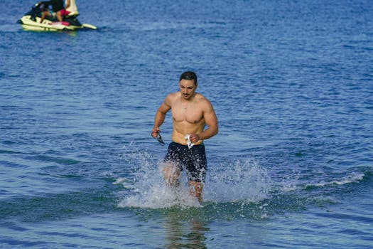 Shirtless man running through shallow water at Kuşadası beach, Türkiye.