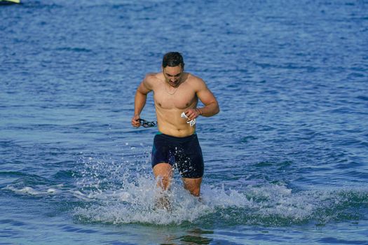 A fit man running out of the sea at Kuşadası beach, showcasing fitness and joy.