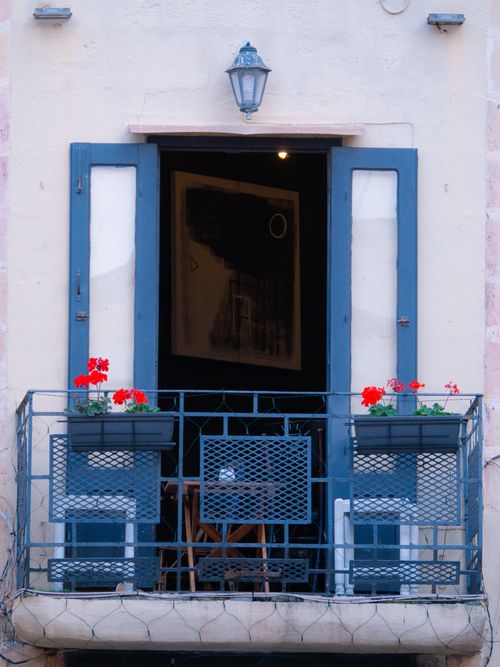 Free Cozy European balcony featuring blue shutters, red flowers, and stylish decor. Stock Photo