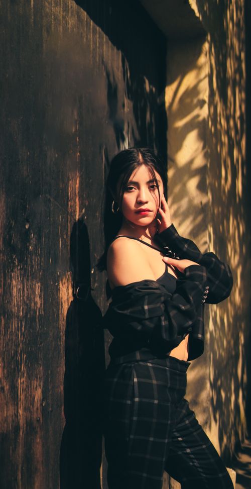 Free Fashionable woman in off-shoulder outfit poses with confident expression against artistic wall under sunlight. Stock Photo