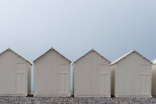 Minimalist image of white beach huts in a row against a clear sky, creating a serene coastal scene.