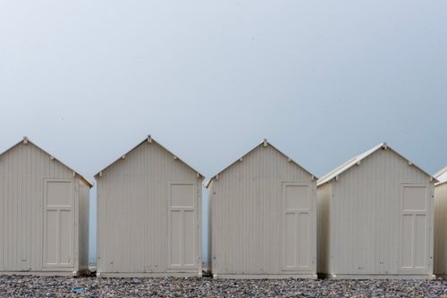 Free Minimalist image of white beach huts in a row against a clear sky, creating a serene coastal scene. Stock Photo