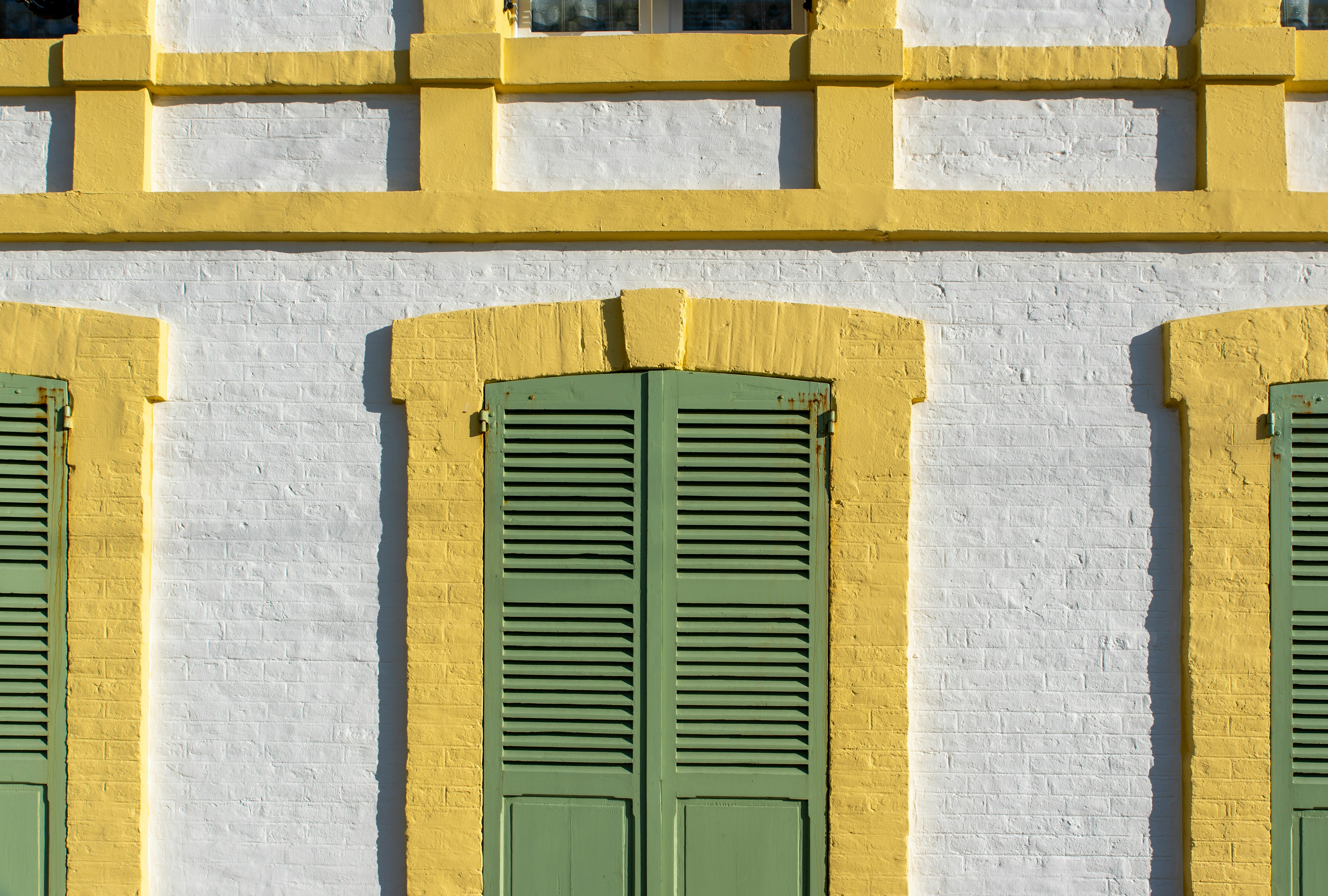 A vibrant building facade with yellow trim and green shutters on white brick. Urban architectural detail.
