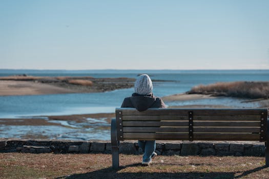 A person in a beanie relaxes on a bench, enjoying a peaceful ocean view at Cove Island Park, Stamford.