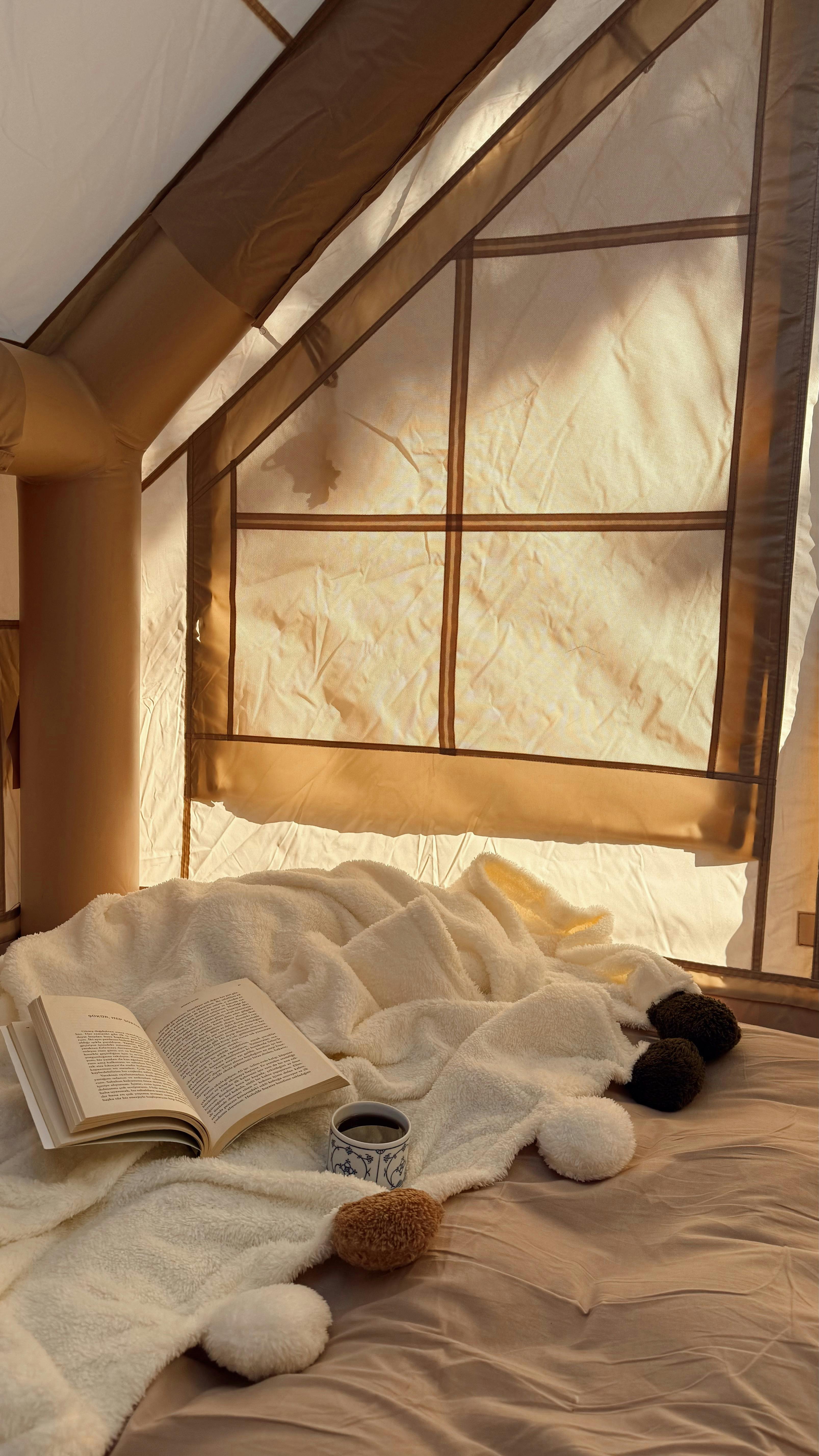 Warm tent interior during daytime with open book and blanket, creating a cozy atmosphere.