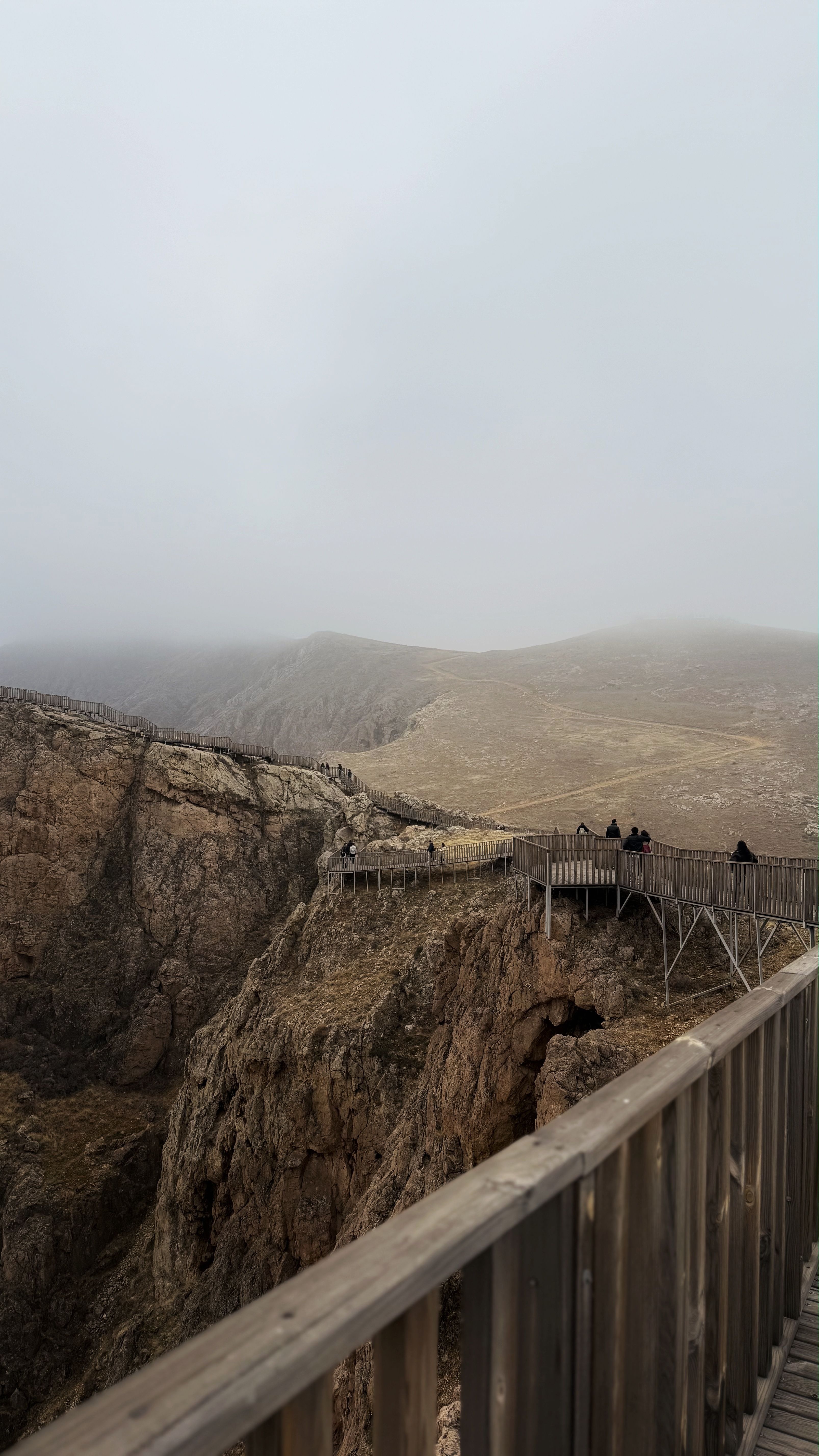 A foggy mountain landscape with an observation deck and distant hikers.
