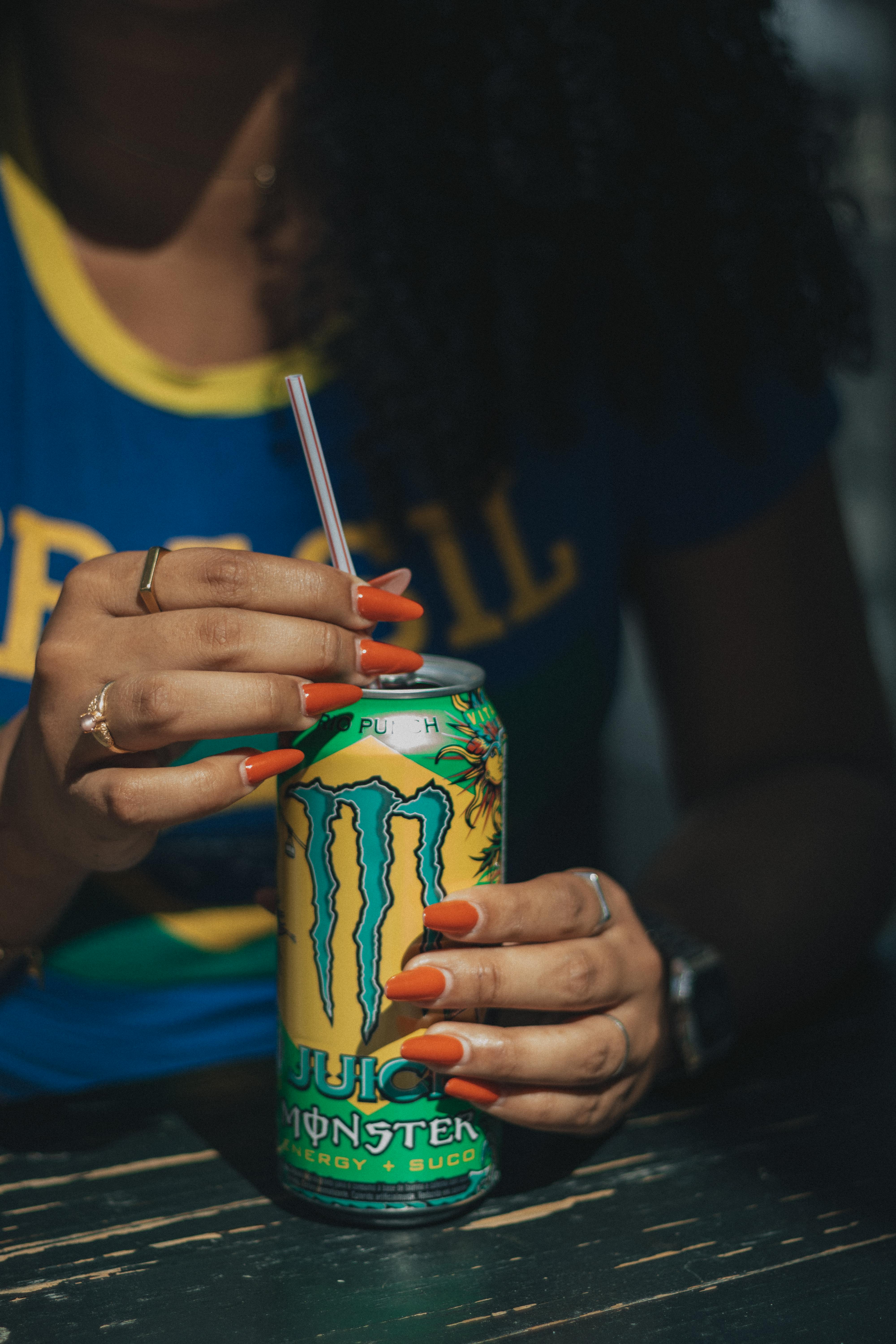Close-up of a person holding a Monster energy drink can with a straw.