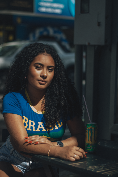 Free Portrait of a young woman in a Brazil shirt sitting at an outdoor café with a drink. Stock Photo
