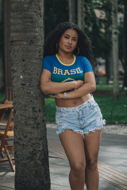 Free Confident woman in Brazil shirt leaning on tree outdoors. Stock Photo