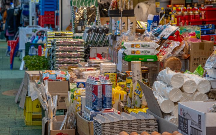 A bustling market aisle filled with various goods including eggs, beverages, and packaged foods.
