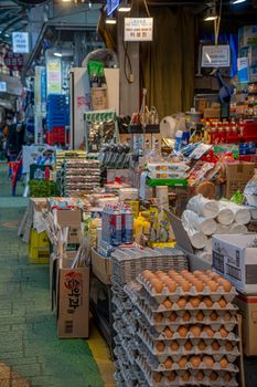A bustling market aisle filled with various goods including eggs, beverages, and packaged foods.
