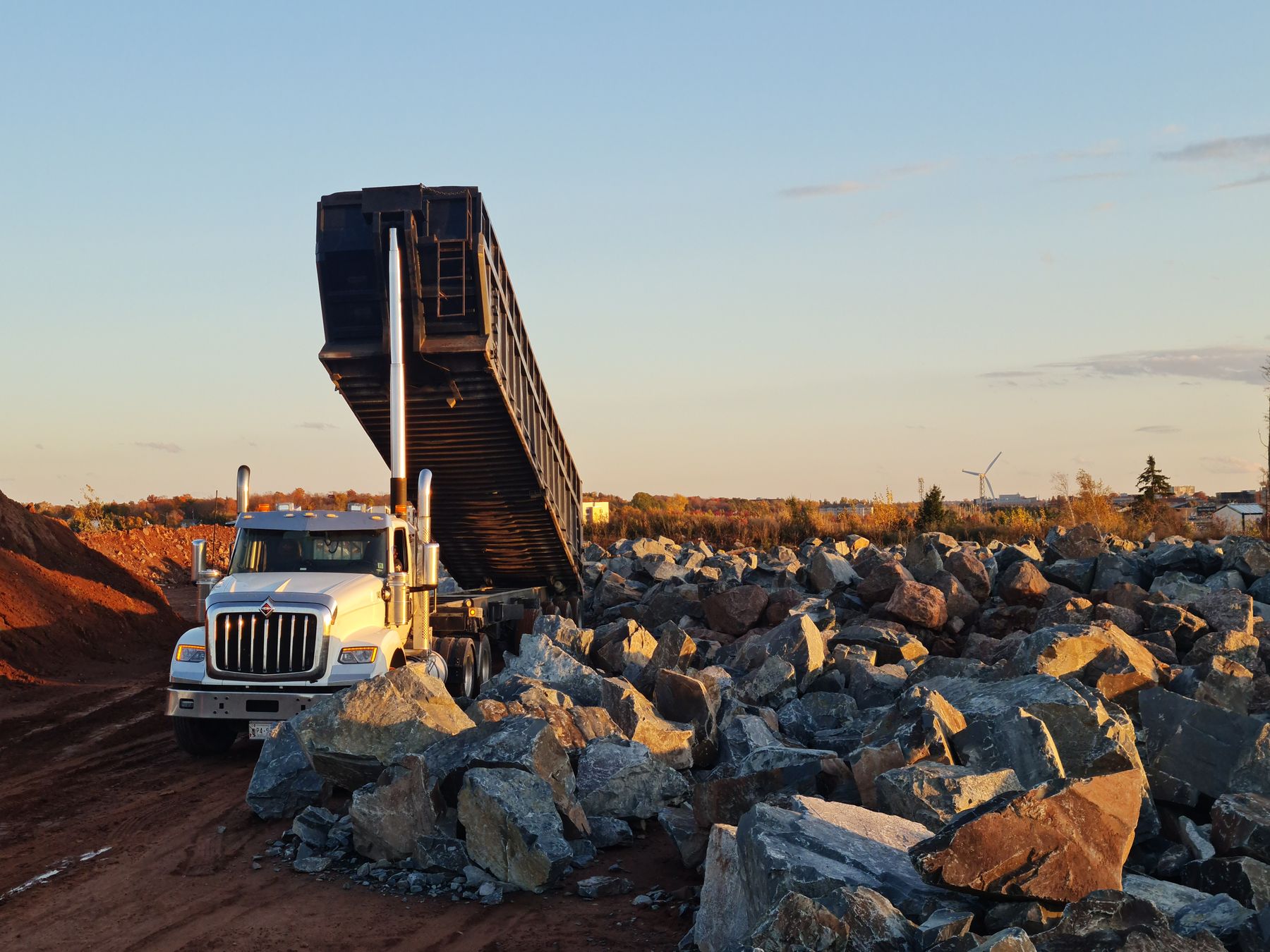 Volqueta descargando roca al atardecer en un frente de acopio