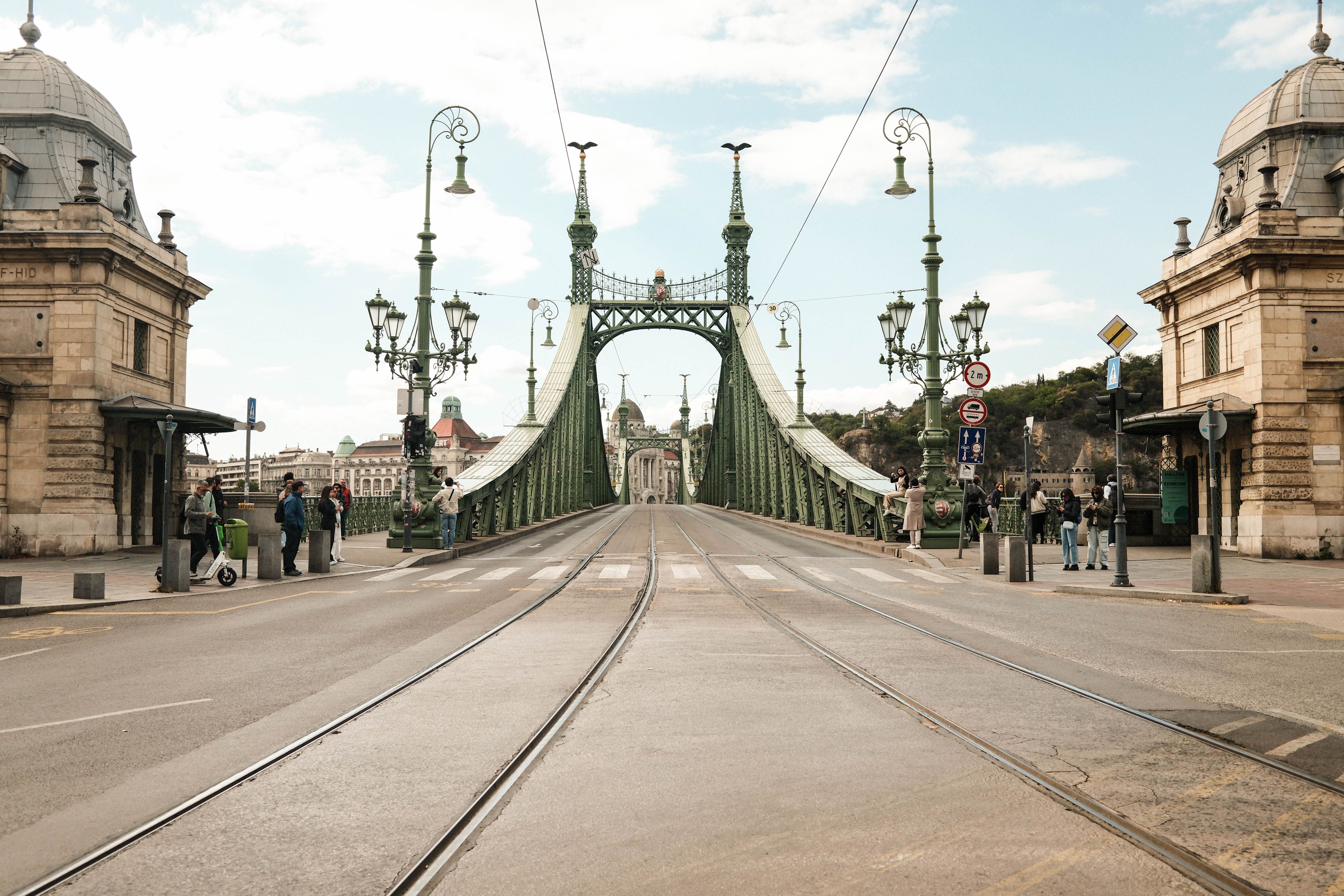 Street view of Liberty Bridge in Budapest during the day, featuring historic architecture and city life.