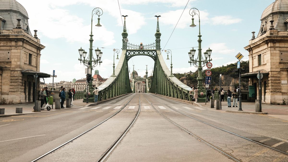Street view of Liberty Bridge in Budapest during the day, featuring historic architecture and city life.
