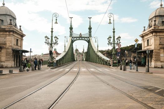 Street view of Liberty Bridge in Budapest during the day, featuring historic architecture and city life.