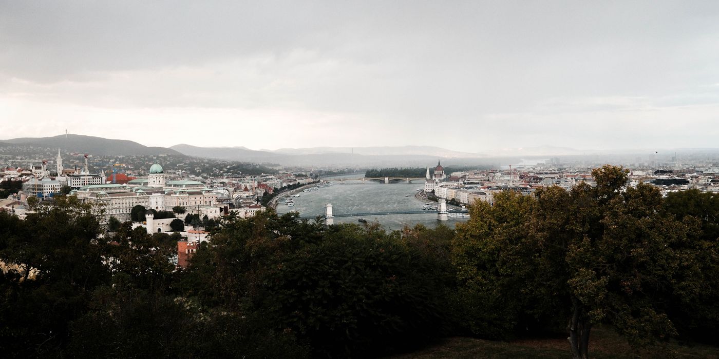 Scenic view of Budapest's cityscape with the Danube River and iconic landmarks under a cloudy sky.