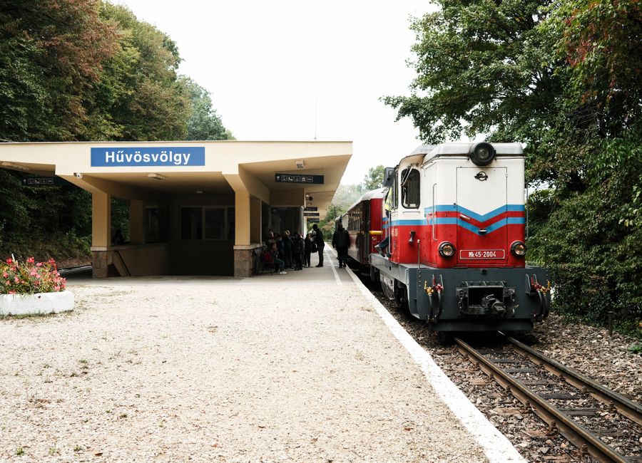 Vintage train at Hűvösvölgy station, Budapest, surrounded by lush greenery. A classic travel scene.