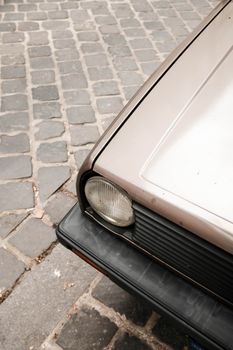 Close-up of a vintage car's headlight on a rustic cobblestone street.