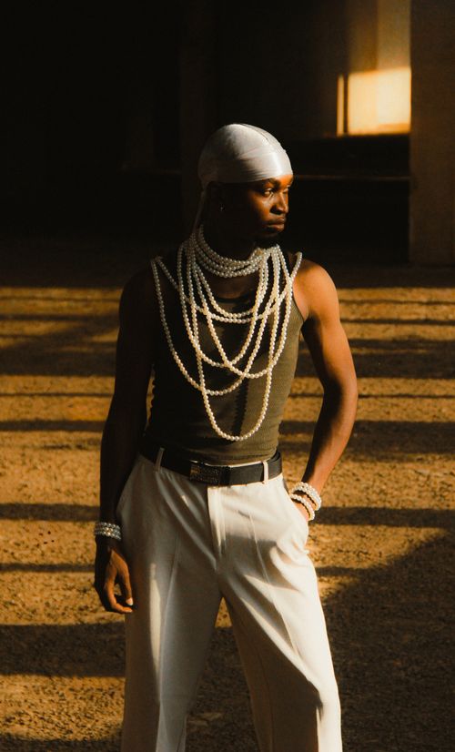 Free Fashionable male model in elegant pearls poses confidently in warm lighting. Stock Photo