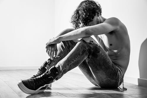 Фотография мужчины топлес, сидящего на полу в оттенках серого