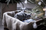 一只毛绒驼鹿玩具被放在圣诞树旁的麻袋内衬板条箱里，营造出舒适的节日氛围