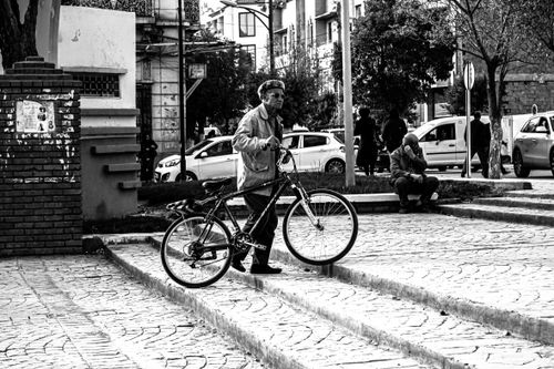 Free Black and white photo of a senior man pushing a bicycle in a city street. Stock Photo