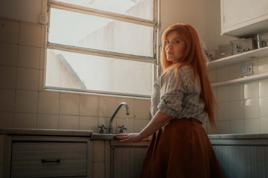 A woman stands thoughtfully in a sunlit kitchen in Buenos Aires, evoking warmth and reflection.