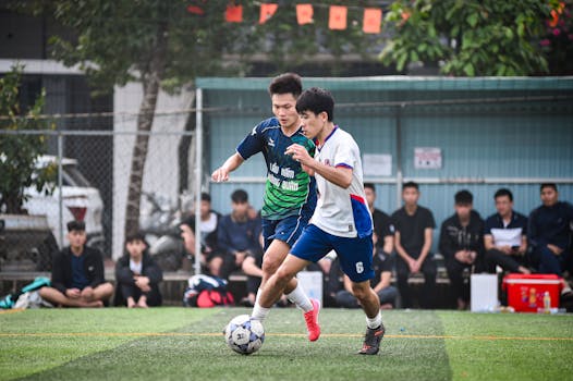 Two players compete fiercely during a football match on a vibrant turf pitch in Hanoi.