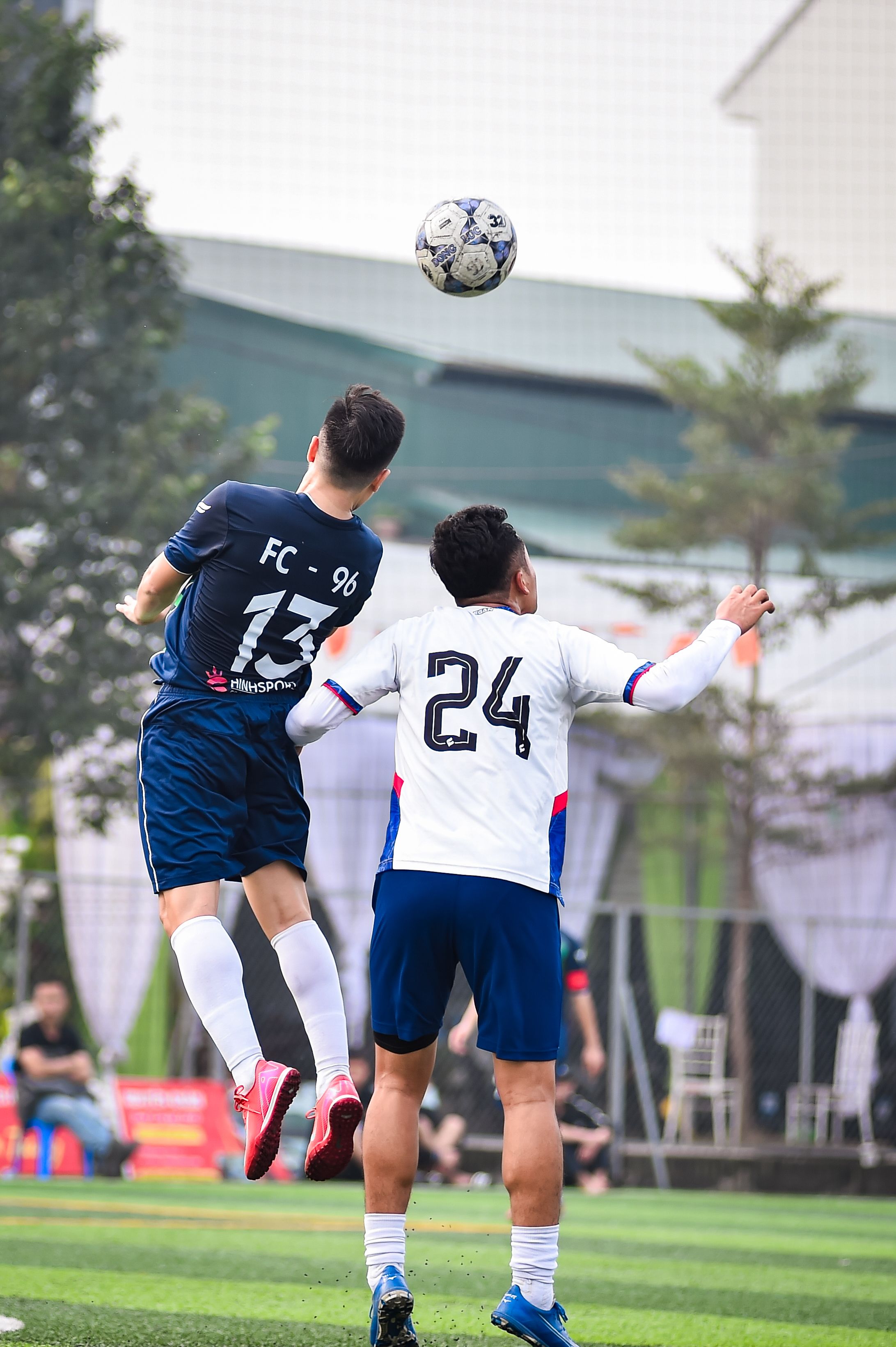 Action shot of two football players jumping for the ball on a sunny day in Hanoi, Vietnam.