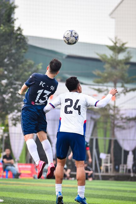 Action shot of two football players jumping for the ball on a sunny day in Hanoi, Vietnam.