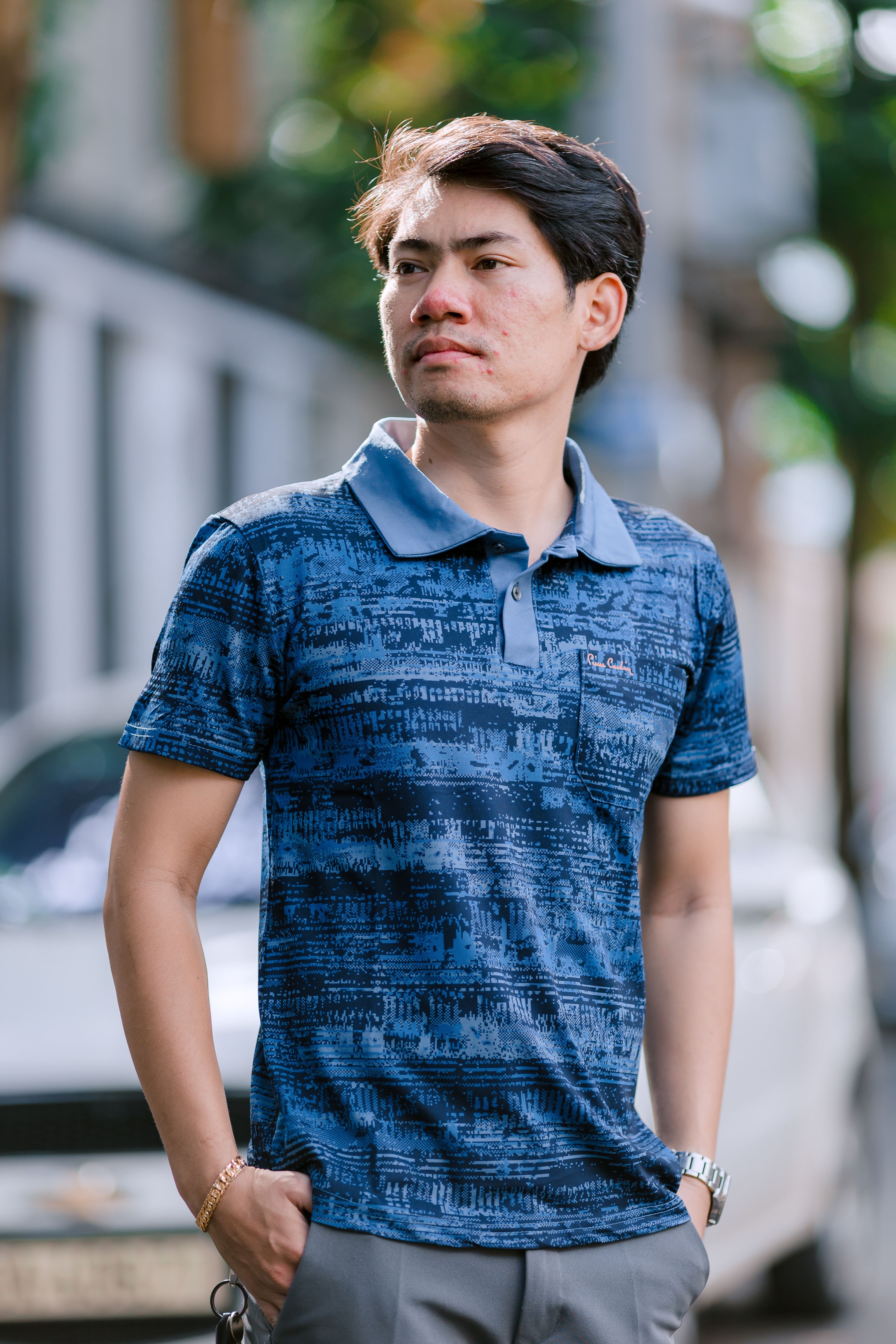 Jovem homem em camisa estampada posando confiantemente ao ar livre.