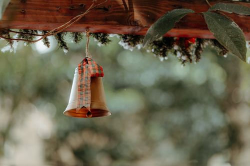 Free A bell with a plaid ribbon hangs under a wooden beam, evoking a rustic and festive atmosphere. Stock Photo