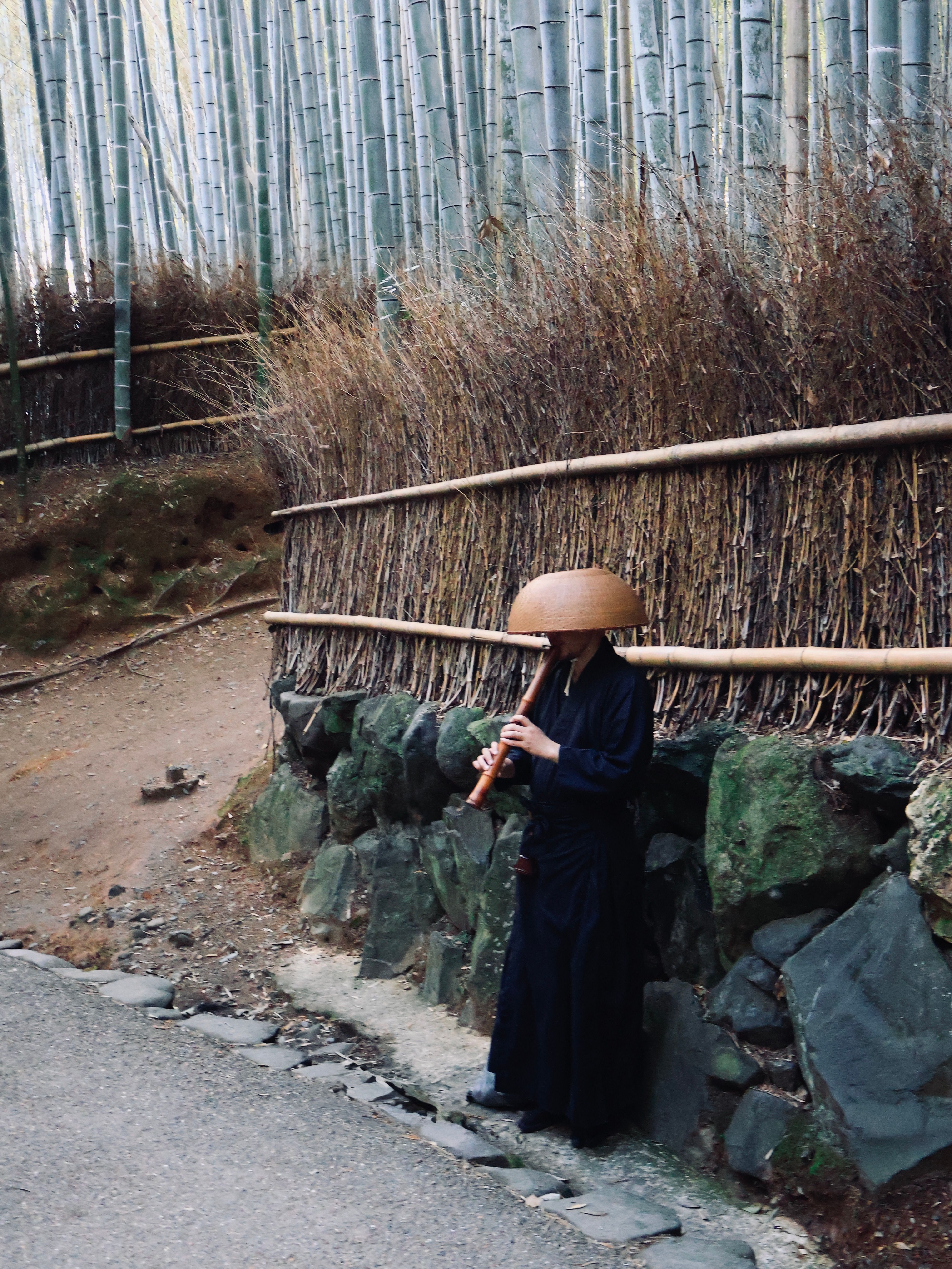 A musician playing a flute in a tranquil bamboo forest setting.