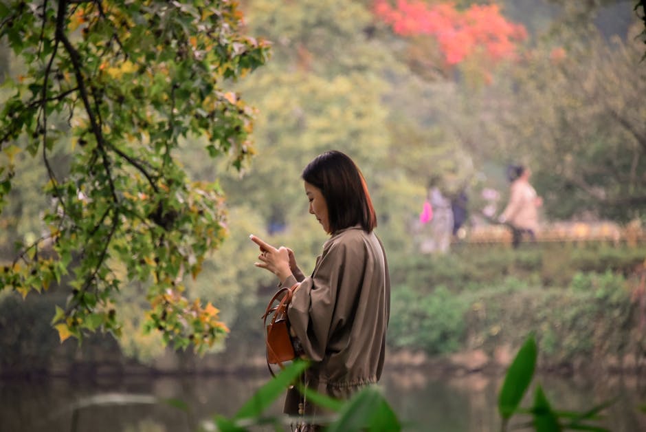 Young woman engrossed in smartphone surrounded by lush greenery in a serene park.