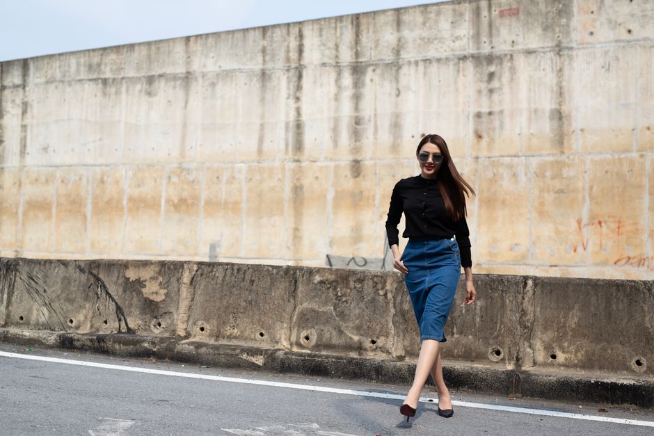 Stylish woman in denim skirt strolling down a city street with concrete wall background.