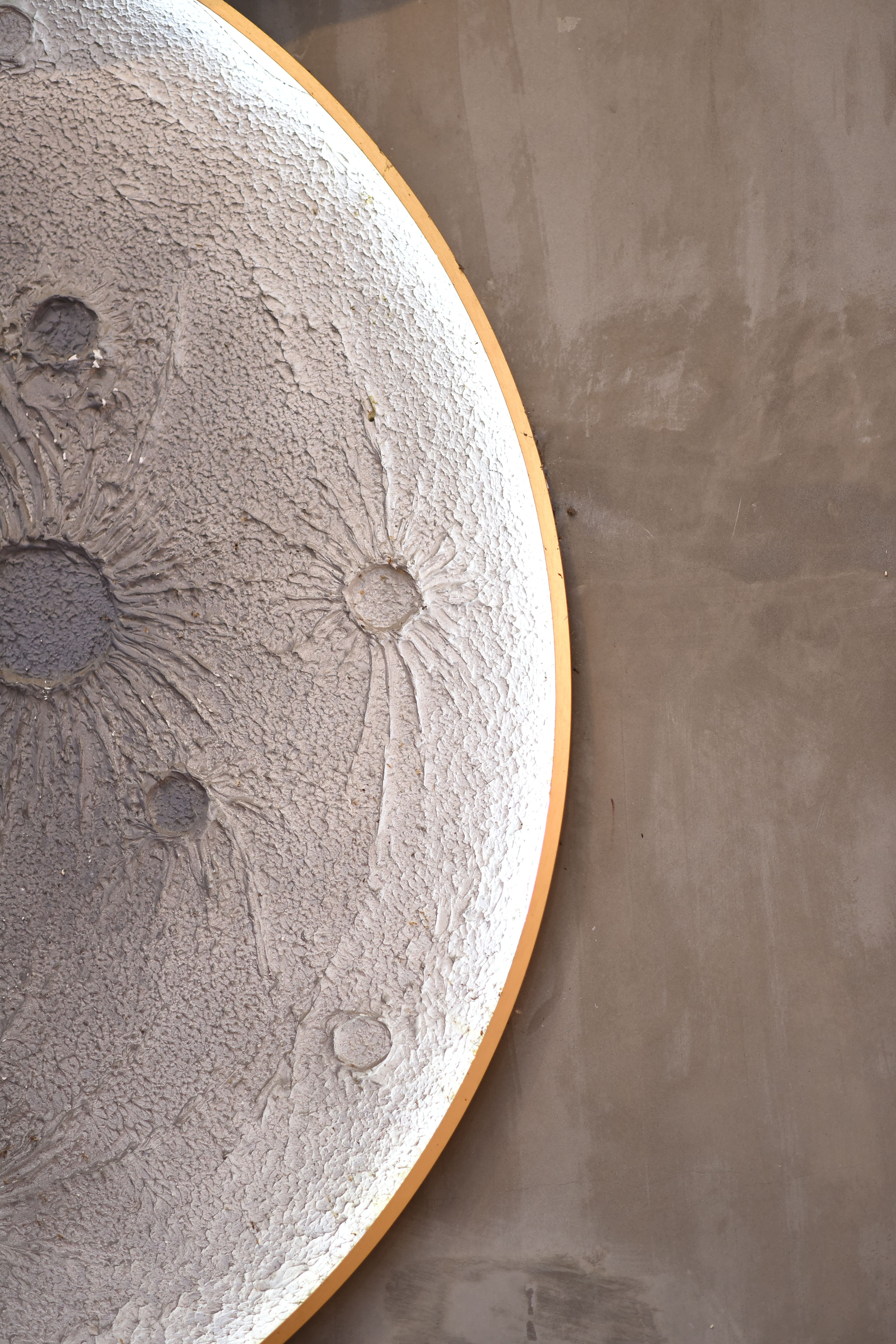 Close-up of a round textured wall art piece resembling lunar craters with concrete background.