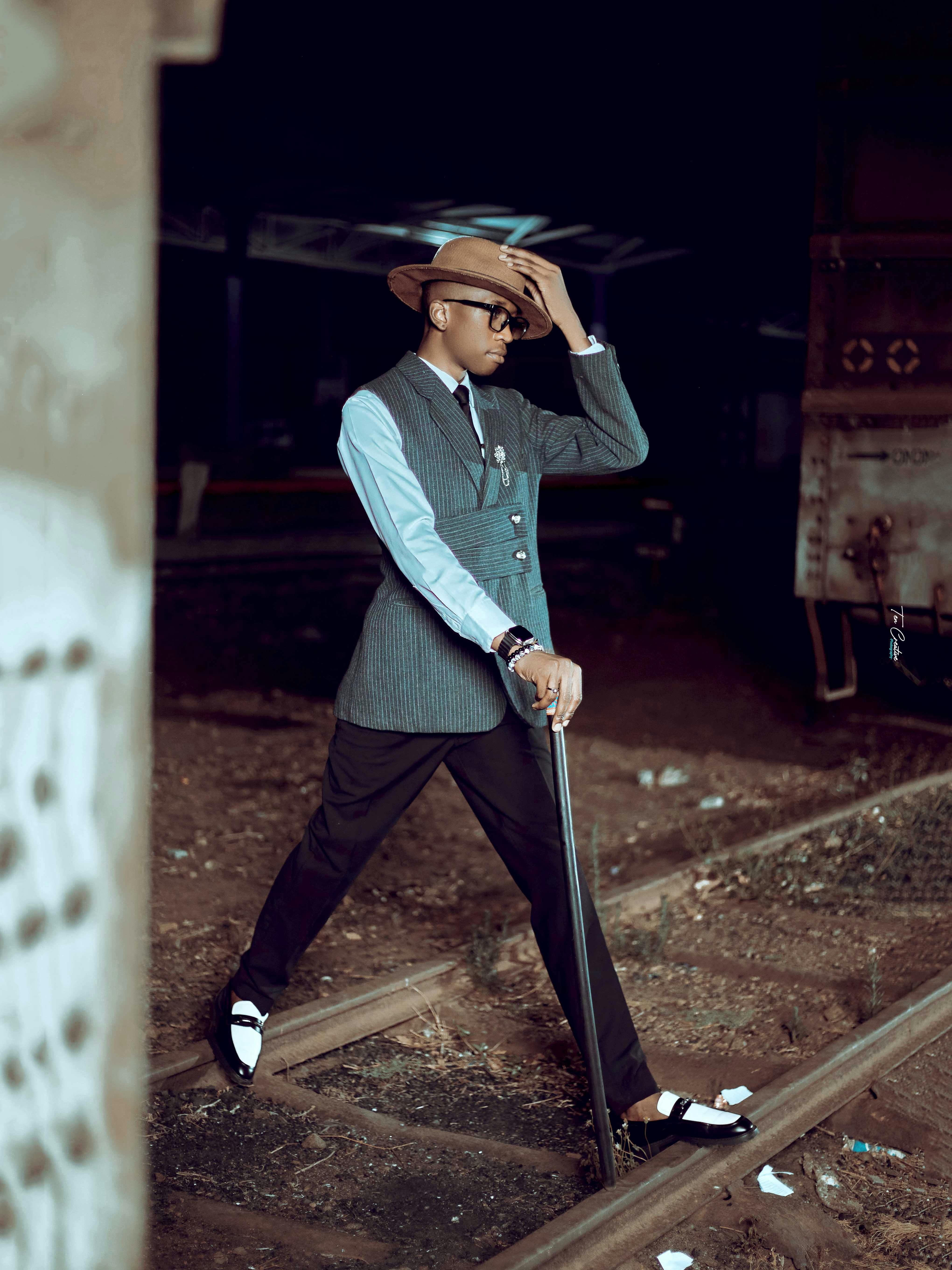 A fashionable man in a vintage suit and hat walks confidently on train tracks, exuding elegance and style.