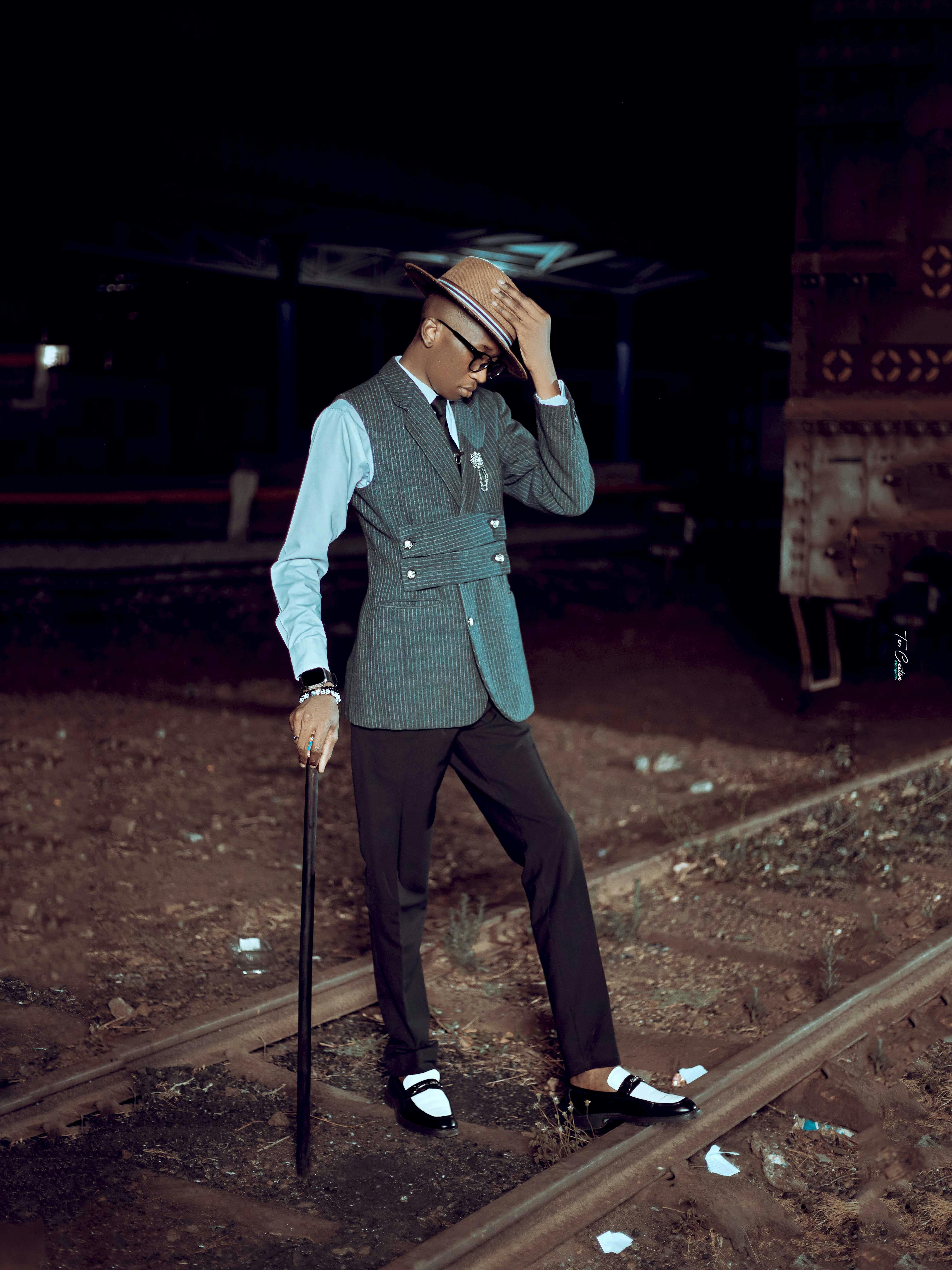 Dapper man in classic vintage outfit poses on railroad at night.