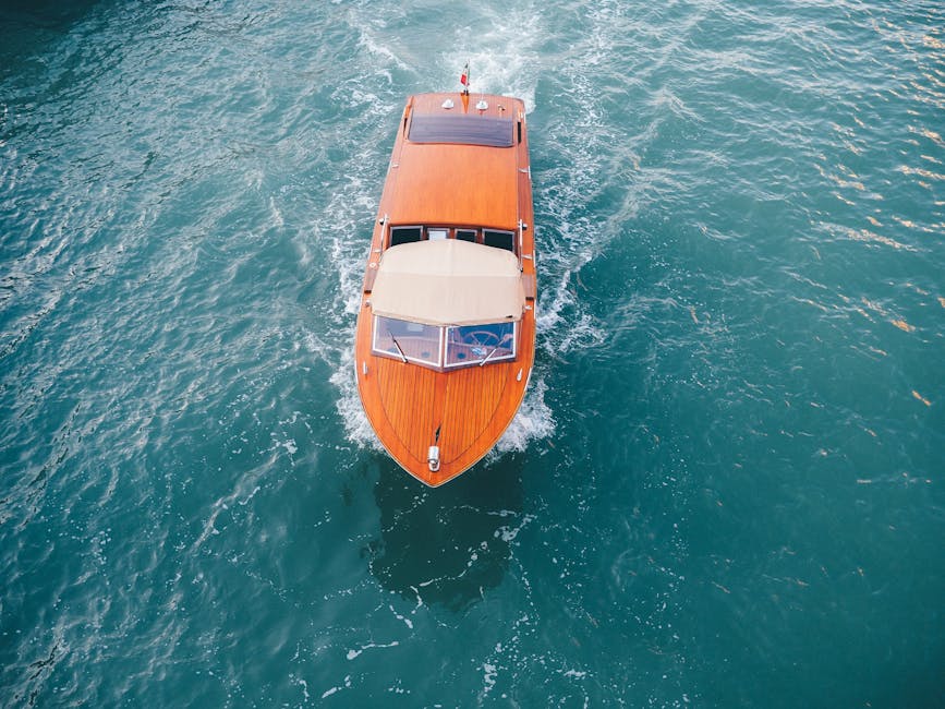 Overhead view of a classic wooden boat navigating the turquoise waters of Venice, Italy.