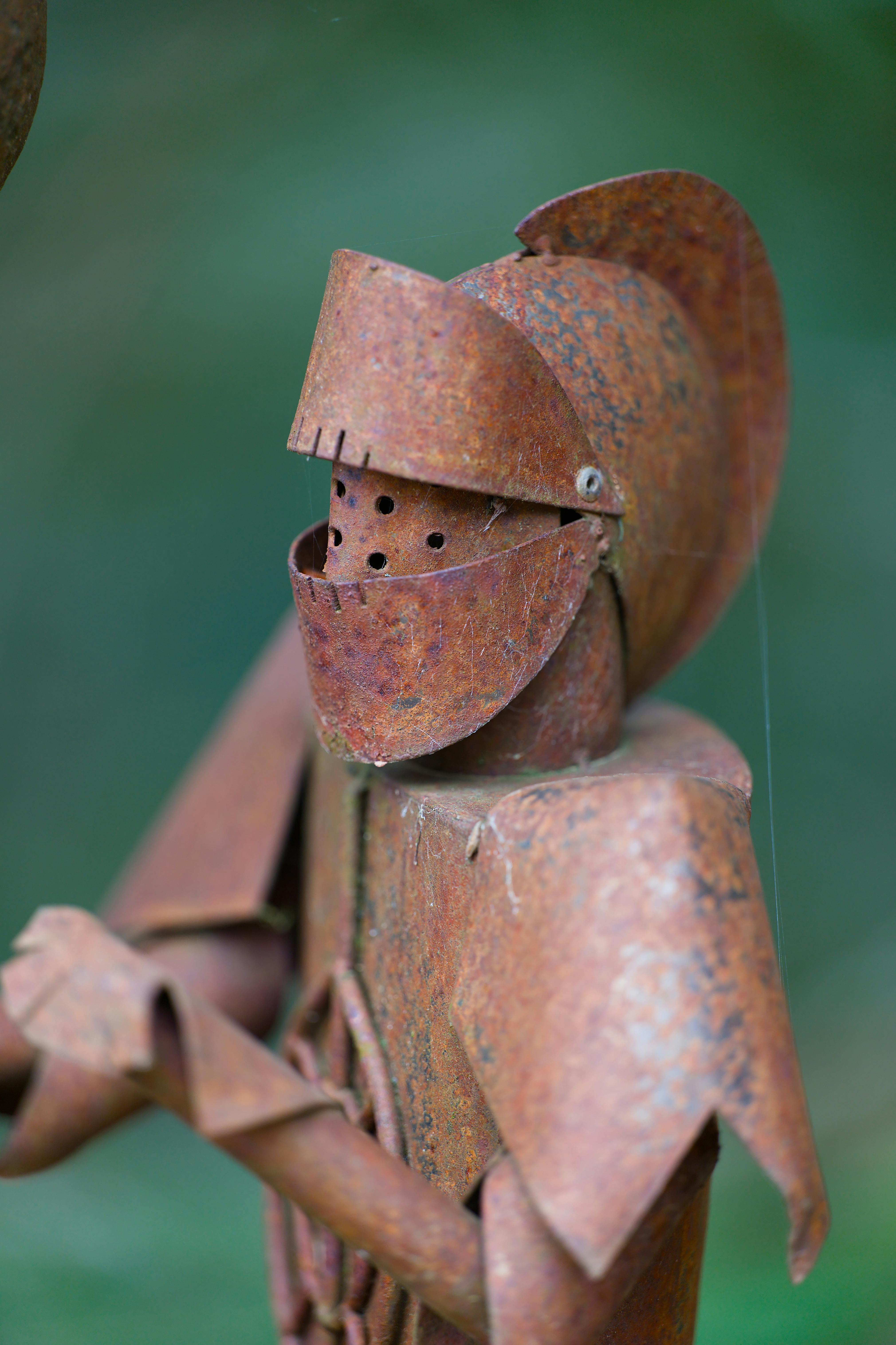 Ücretsiz Paslı metalden yapılmış bir şövalye heykelinin yakın çekim görüntüsü, bulanık bir orman arka planı önünde ortaçağ havası uyandırıyor. Stok Fotoğraflar