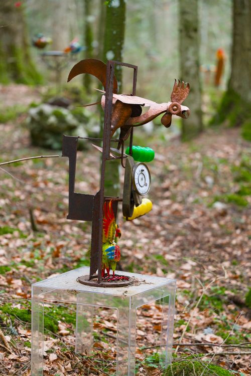 Free Colorful metal rooster sculpture on clear stand in a forest clearing. Stock Photo