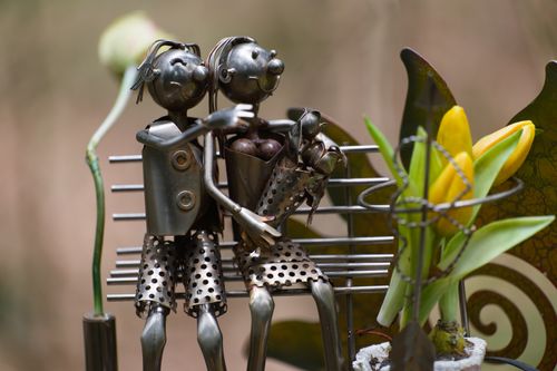 Free Creative metal sculpture of a family on a bench with flowers in an outdoor setting. Stock Photo
